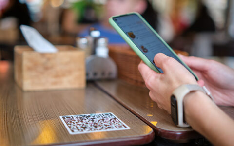 Closeup of guest hand ordering meal in restaurant while scanning qr code with mobile phone for online menu